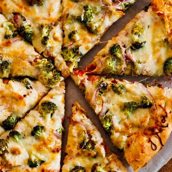 A whole pizza with broccoli and red onions, cut into slices, on parchment paper and a wooden board.