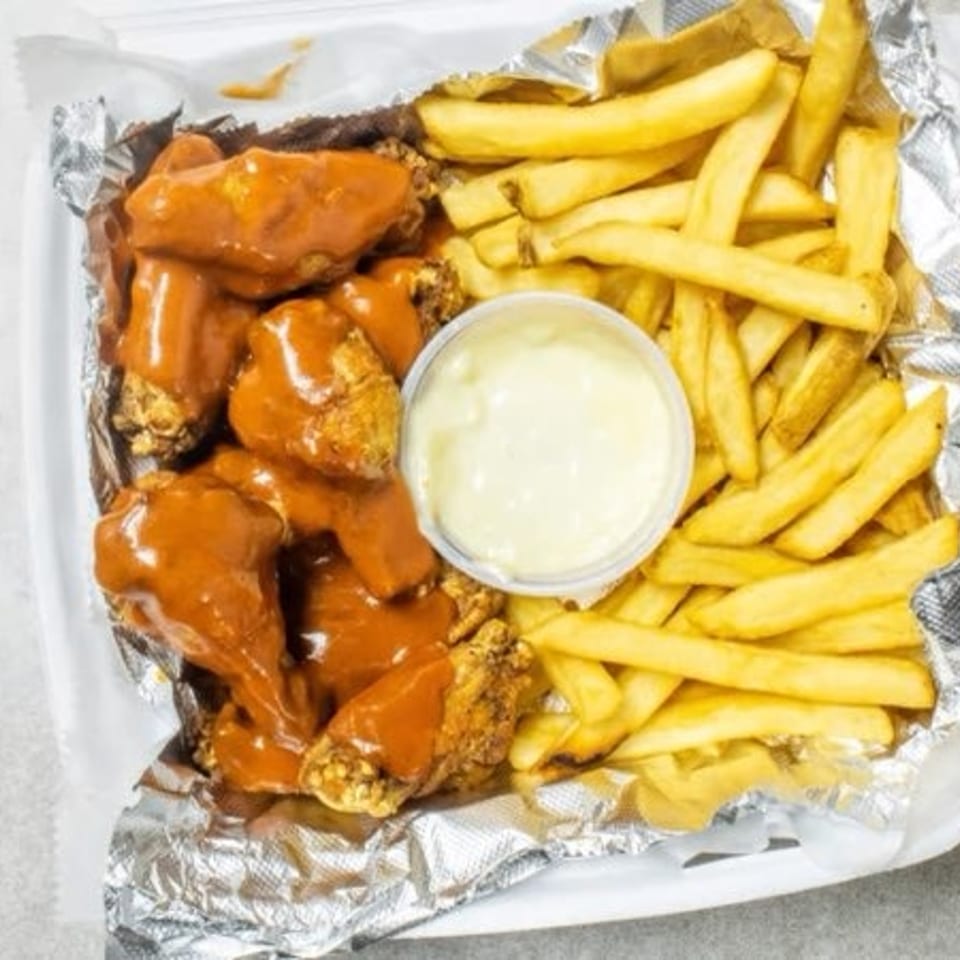 A takeout container filled with buffalo wings, golden french fries, and a side of dipping sauce.