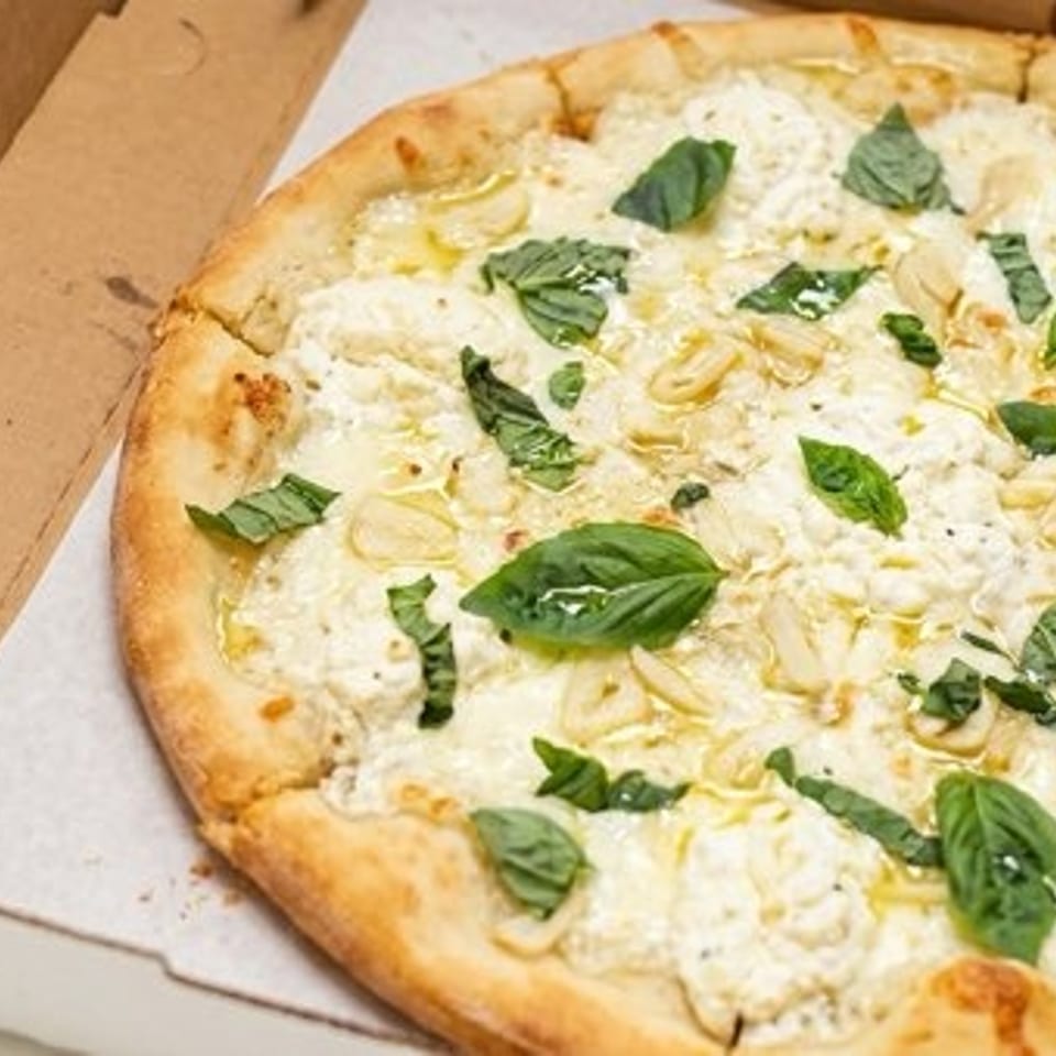 White pizza with ricotta, sliced garlic, and fresh basil leaves in an open pizza box.