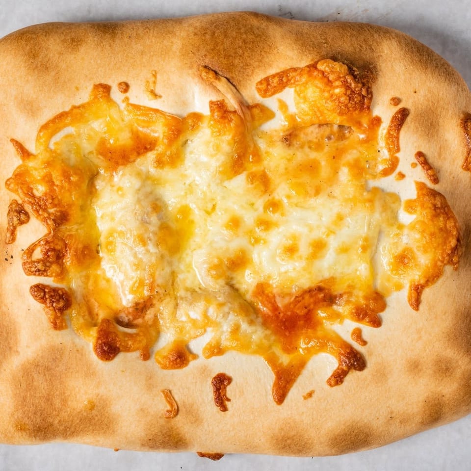 Golden-brown calzone with melted, bubbly cheese on top, viewed from directly above.