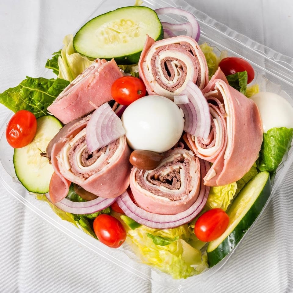 A chef salad with rolled deli meats, hard-boiled eggs, tomatoes, cucumbers, and red onions.